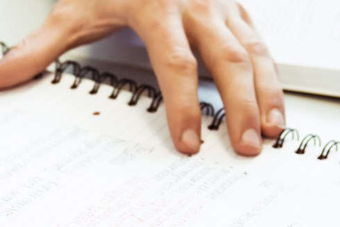 A close up of a pair of hands writing in notepad and open text book