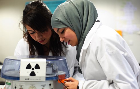 Two females in white lab coats working with some science equipment.