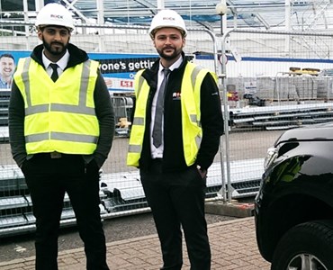 Two men in high visibility jackets stood next to electric car
