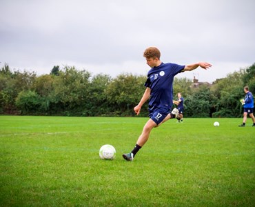 Male student in a blue football kit about to kick a football  