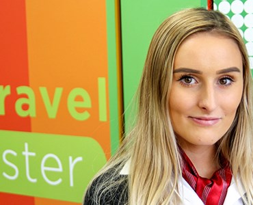 Female Travel and Tourism student stood in front of the Spires Travel Worcester logo