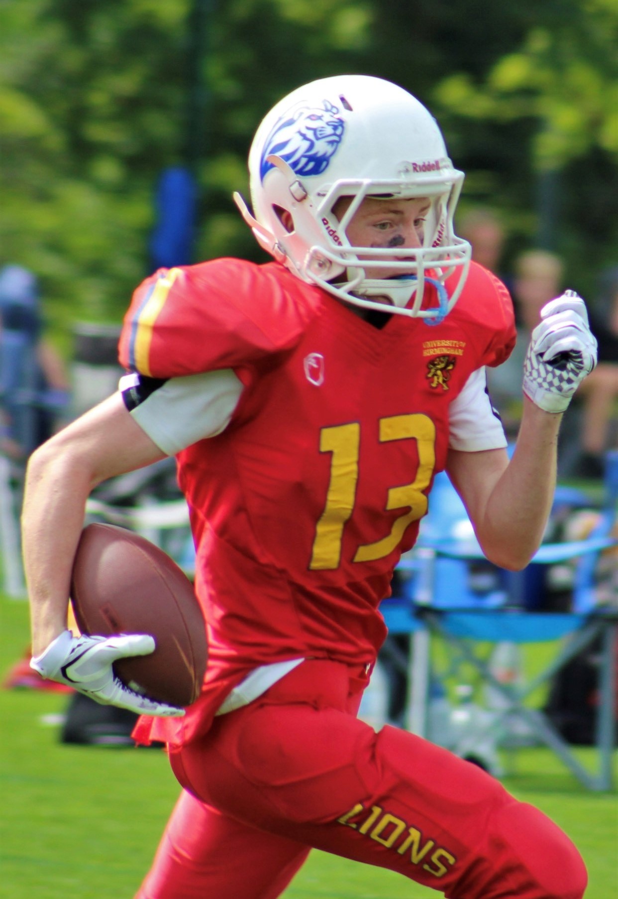 Male American football player running in red uniform whilst holding the ball