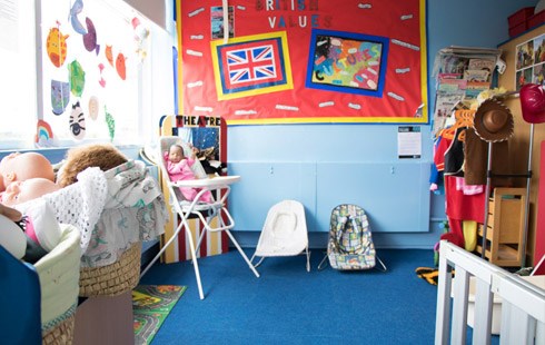 Picture of health and social care classroom; children's toys, clothes and bright colourful wall art.