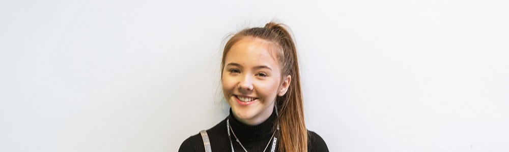 Female student with ponytail smiling in front of a white wall