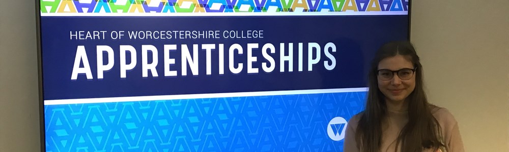 Female student stood in front of large TV with the Heart of Worcestershire College Apprenticeships logo on