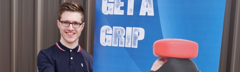 Male smiling in front of Get a Grip banner whilst holding a grip device in the palm of his hand