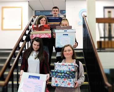 5 students stood on the stairs whilst holding colourfully wrapped boxes