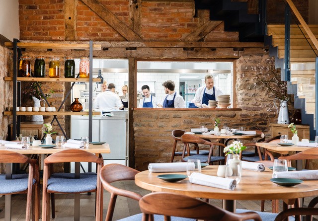 Photo taken inside a converted barn home to the Pensons restaurant. Tables and the kitchen are visible.