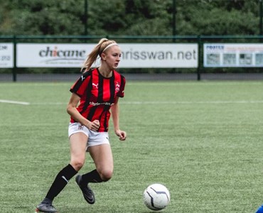 Female playing football in red and black stripe jersey