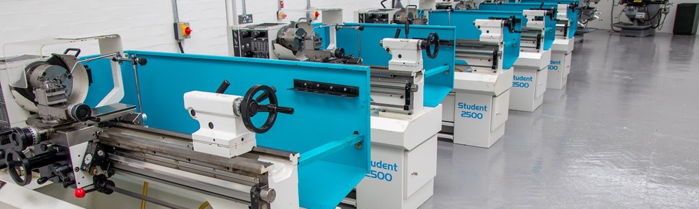 Row of grey and light blue machines in an engineering workshop.