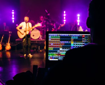 A close up of a music sound engineering screen with student in a band playing on stage in the background