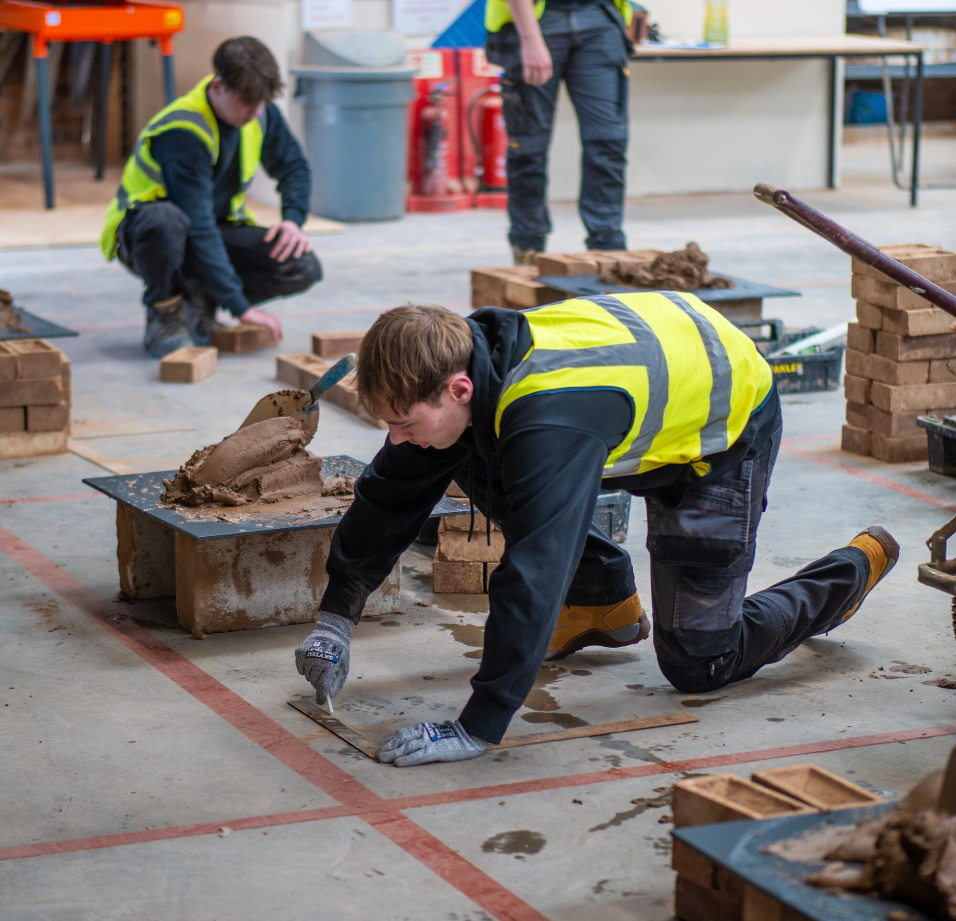 Two students knelt down doing bricklaying in the Colleges construction facilities