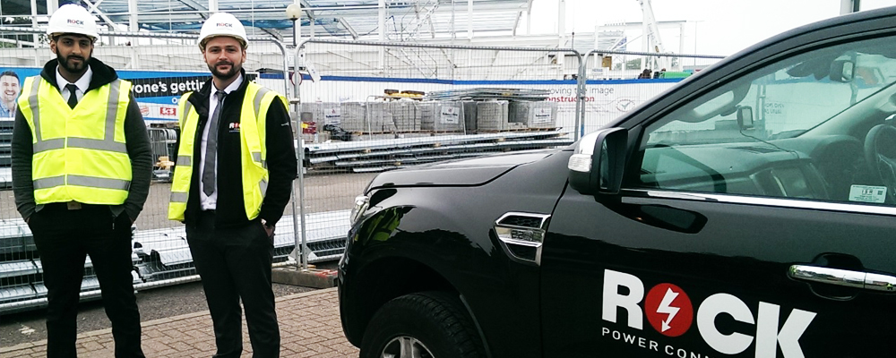 Two men in high visibility jackets stood next to electric car