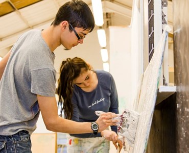 Male and female student painting a wall together.