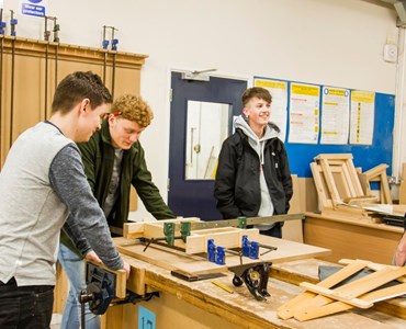 Group of male students smiling around a woodwork desk 