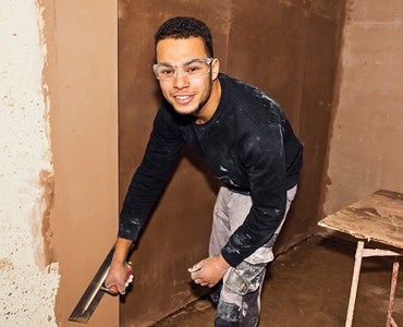 Male student smiling while plastering a wall
