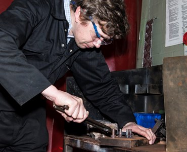 Male student working on metal in black overalls and protective goggles