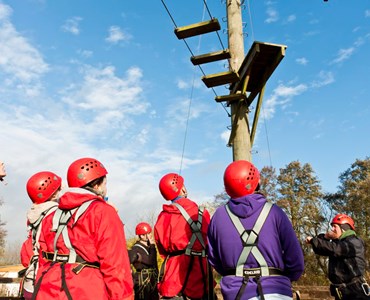 Group of students in red helmets and harnesses at high ropes course.