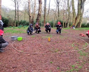 Group of students outside in a woodland and completing team building exercises with ropes.