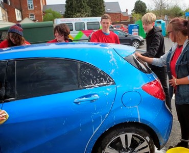 Group of students in red tshirts washing a blue car.
