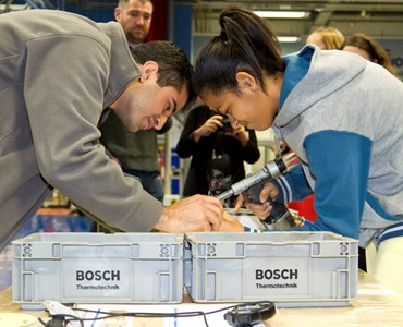 Male and female student working opposite each other at desk with tools; two boxes present that read 'Bosch'