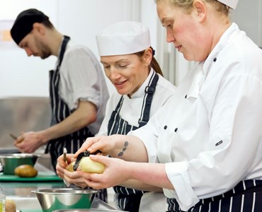 3 students in chef whites peeling potatoes.