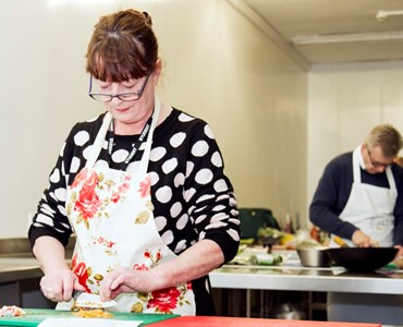 Mature female student wearing an apron and chopping vegetables.