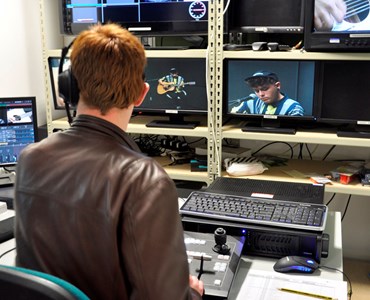A student facing away from the camera sat in a TV recording studio with several TV screens and studio equipment