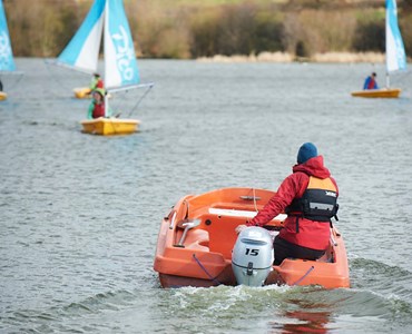 A group of students wind sailing with a lifeguard boat next to them