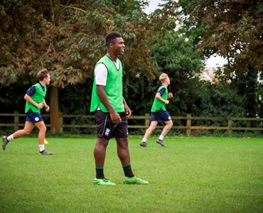 3 male students in green and blue football kit playing football