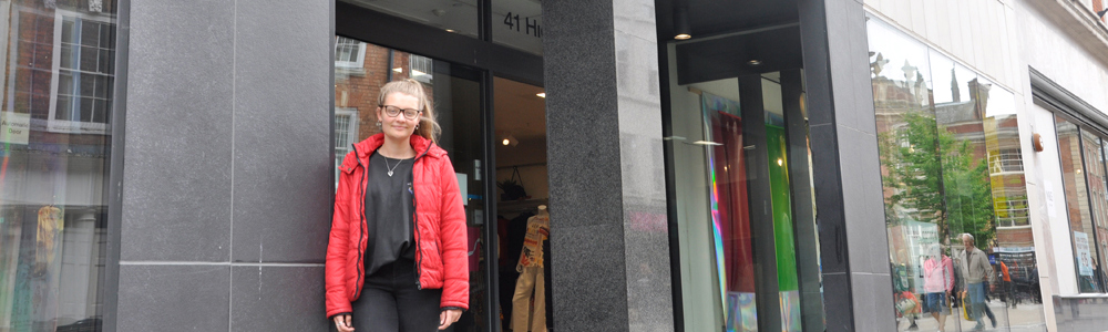 Female student stood in front of big grey fashion building