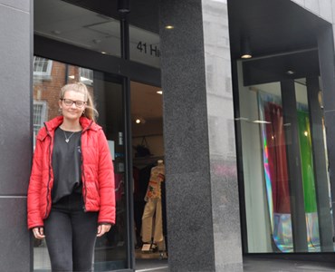 Female student stood in front of big grey fashion building