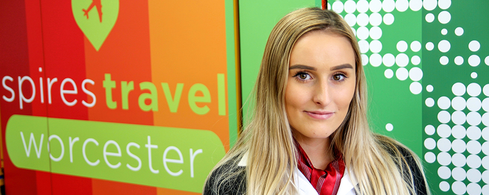 Female Travel and Tourism student stood in front of the Spires Travel Worcester logo
