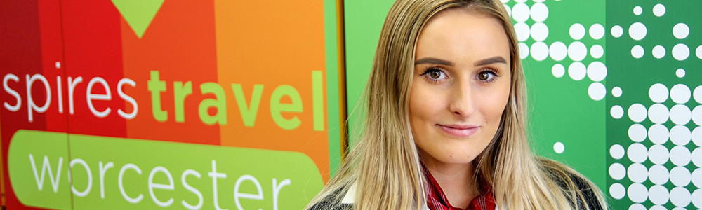 Female Travel and Tourism student stood in front of the Spires Travel Worcester logo