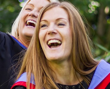 A close up of two female students in graduation robes, smiling and laughing
