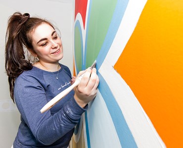 A close up of a female student painting an artistic design on a wall