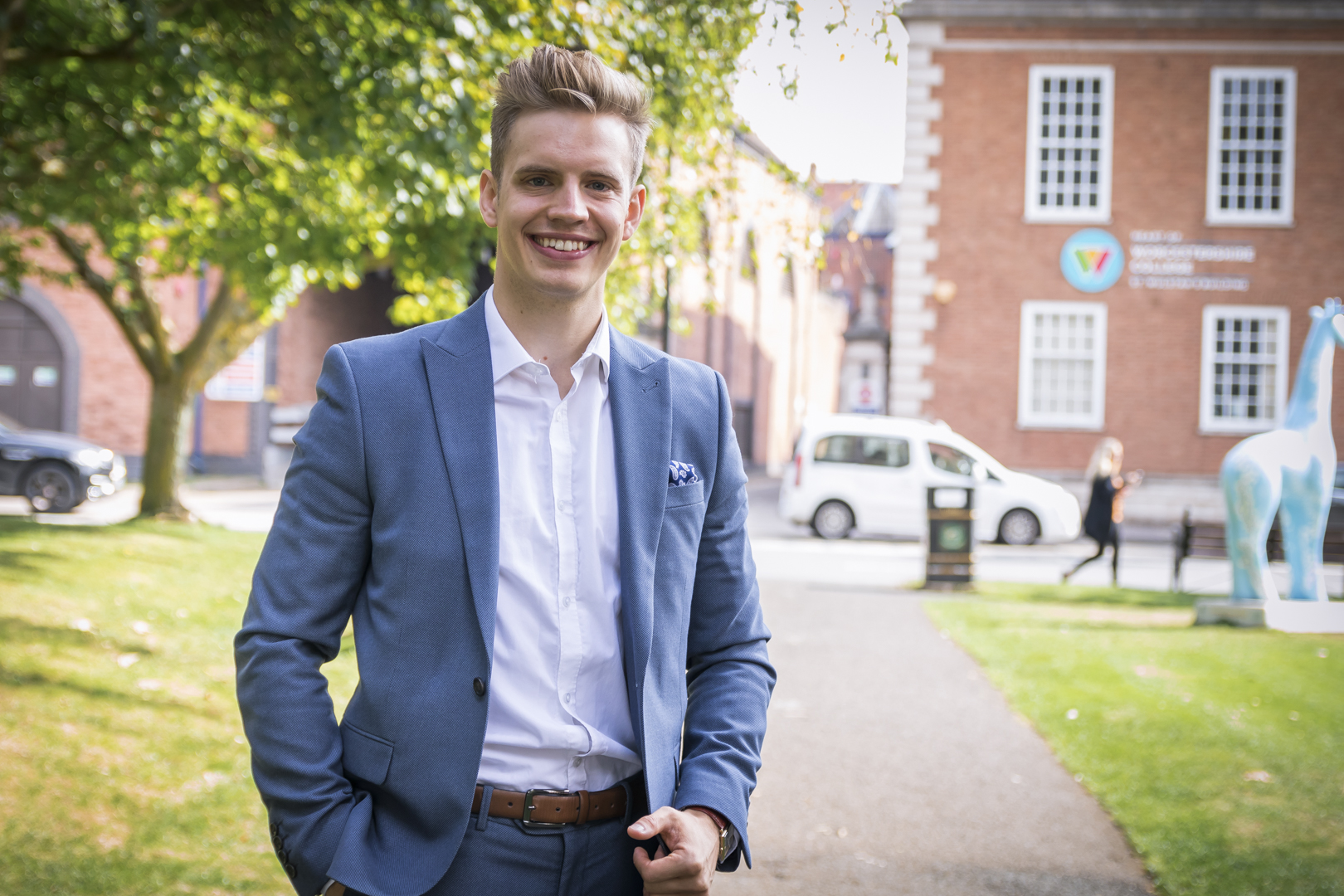 Male former student wearing a grey-blue suit stood outside of HoW College building