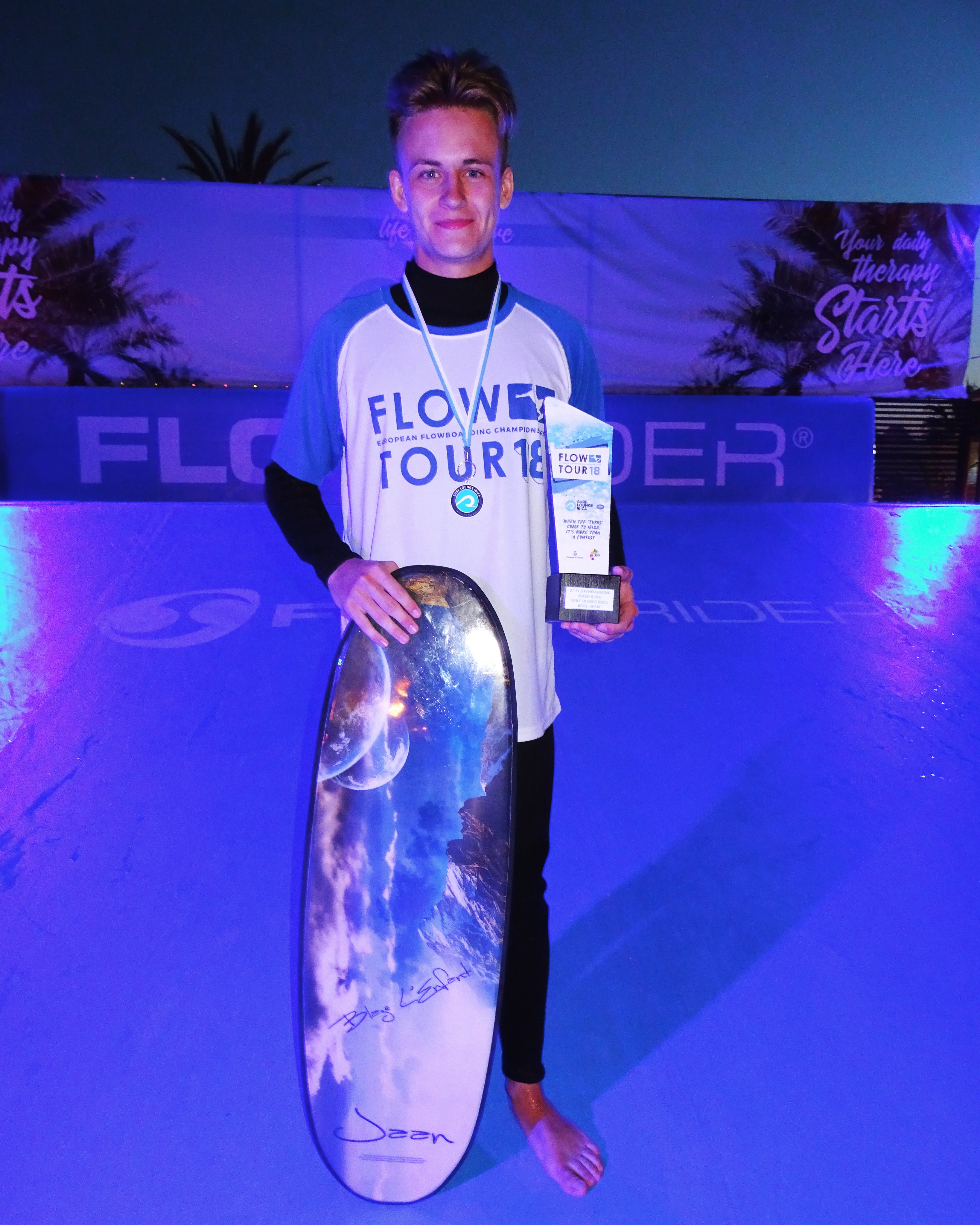 Male student wearing a medal, holding an award and holding a flow rider board