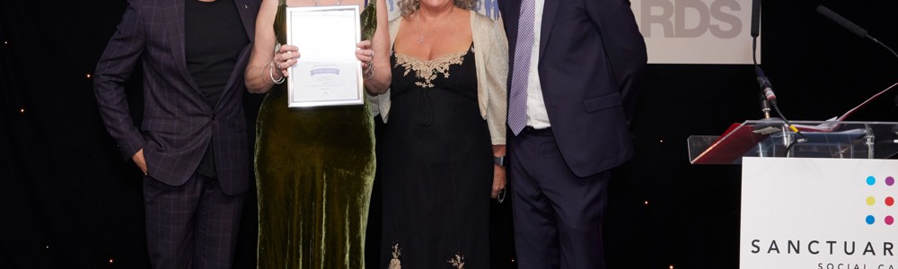 2 female adults and 2 male adults smiling and holding certificate at an awards evening