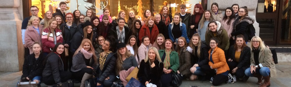 Large group of students smiling and stood outside in front of big shop during winter