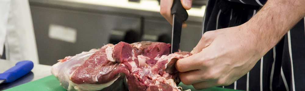 A chef's hand slicing a large piece of red meat with a knife on green chopping board