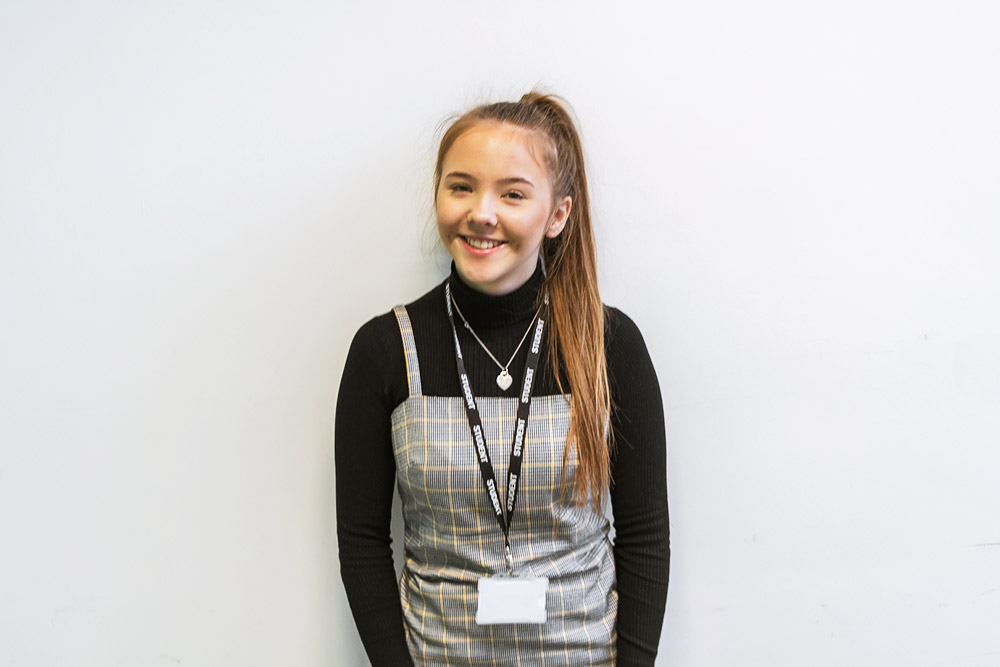 Female student with ponytail smiling in front of a white wall