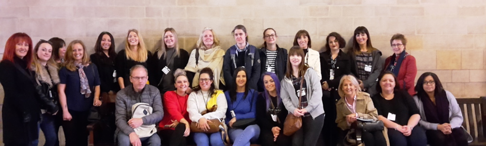 Large group of students and staff smiling in front of stone wall