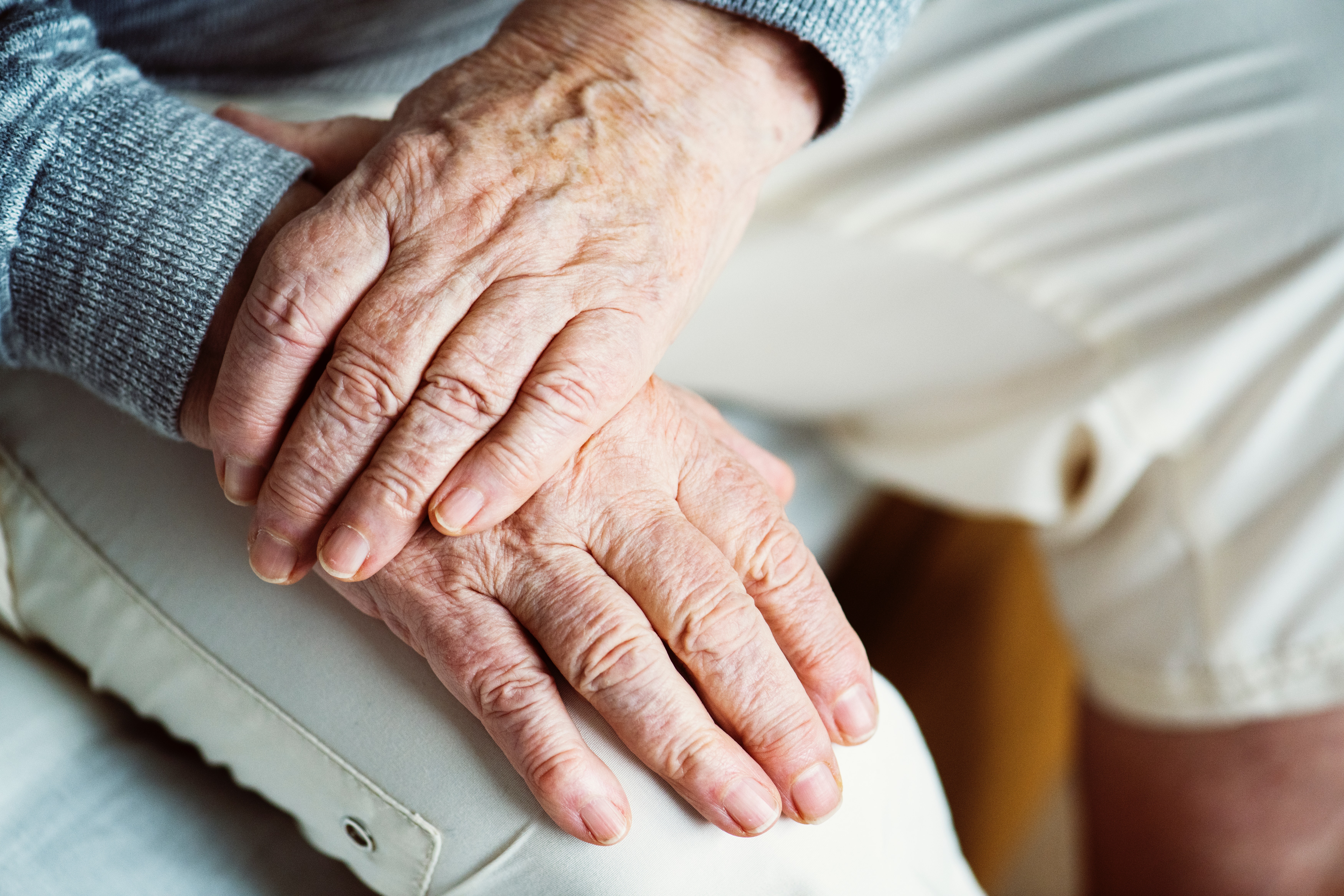 Old male hands placed on top of one another whilst resting on a knee.