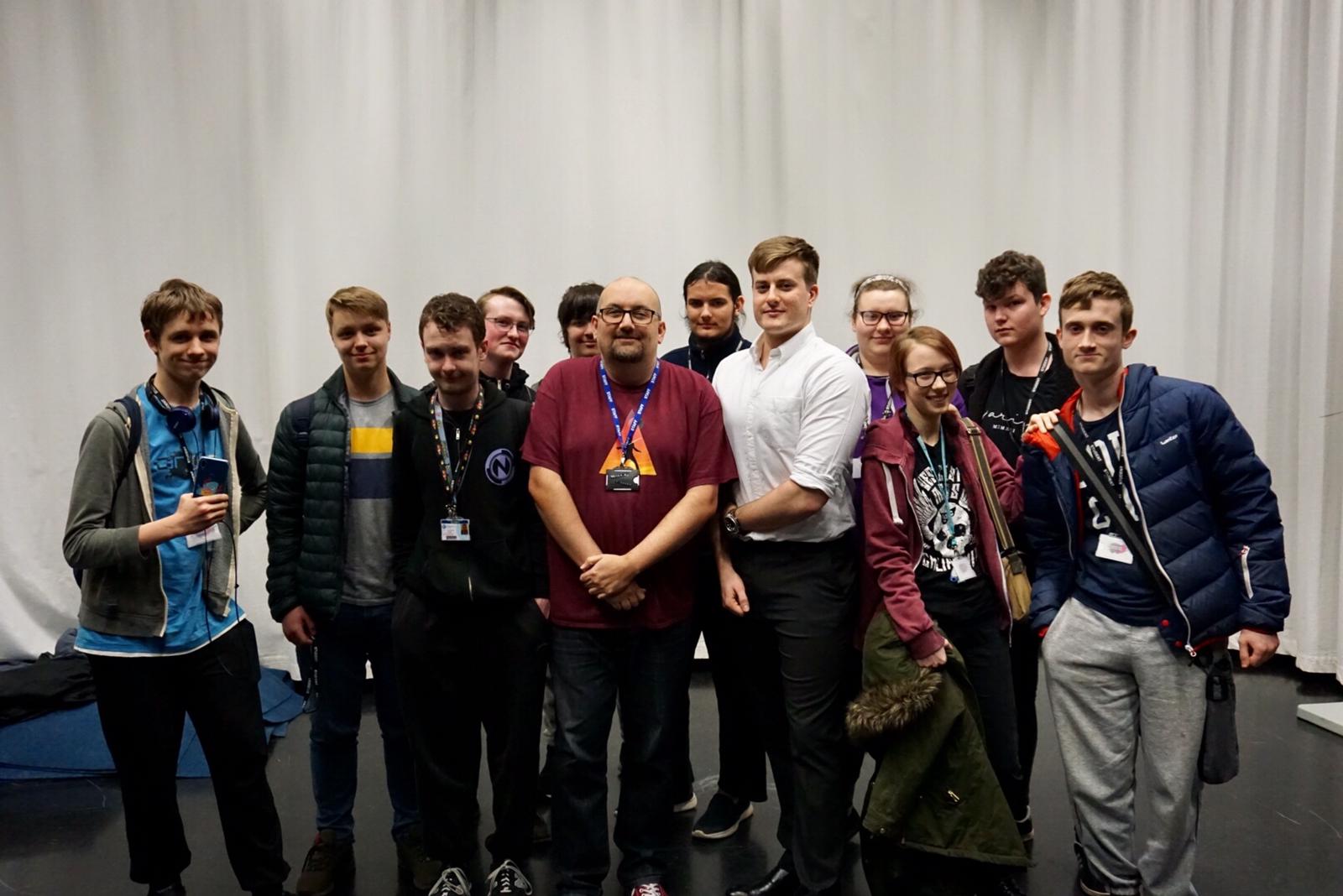 Large group of computing students stood smiling in front of white drapes