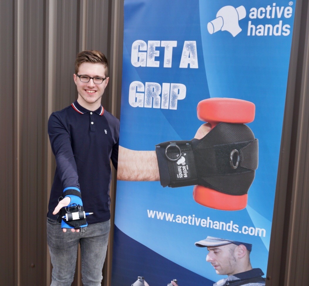 Male smiling in front of Get a Grip banner whilst holding a grip device in the palm of his hand