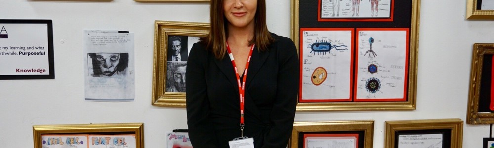 Female stood smiling in front of white wall holding art work in golden frames