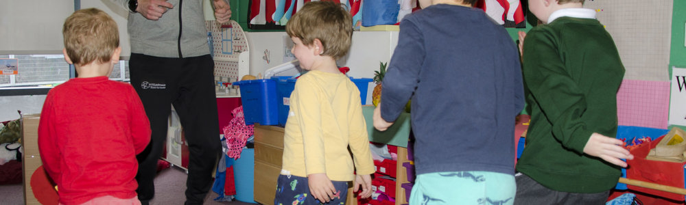 Male teacher stood in front of 4 male children in a classroom