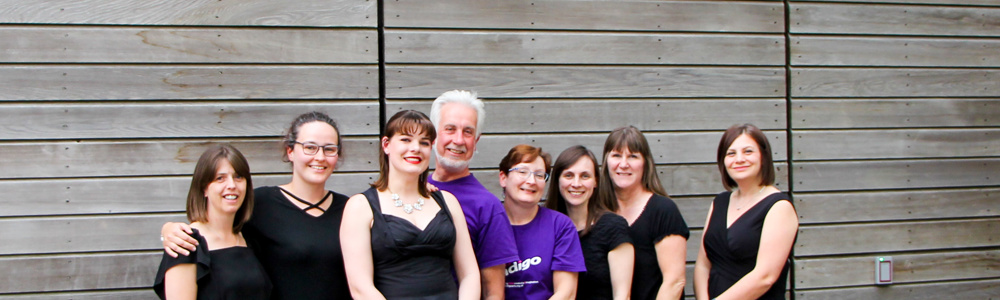 Group of adults dressed smartly in black and purple. Stood smiling underneath Archer's Restaurant sign outside.