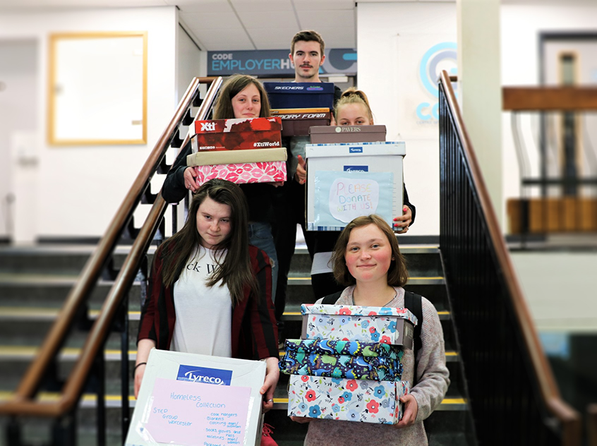 5 students stood on the stairs whilst holding colourfully wrapped boxes